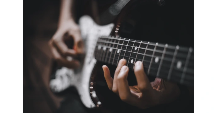 vue de mains qui jouent sur une guitare électrique noire et blanche